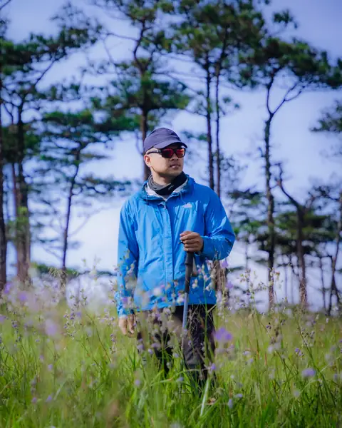 นักเดินป่าเสื้อแจ็กเก็ตสีฟ้ายืนกลางทุ่งดอกหงอนนาค