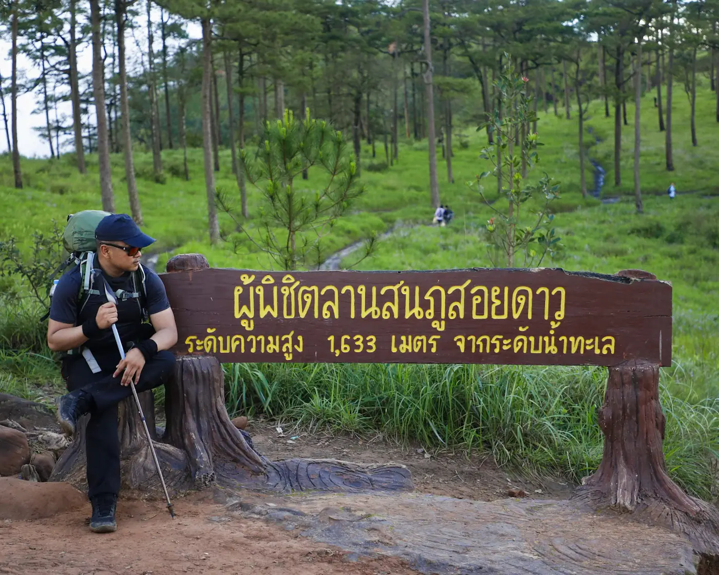 นักเดินป่านั่งข้างป้ายผู้พิชิตลานสนภูสอยดาว ระดับความสูง 1,633 เมตร